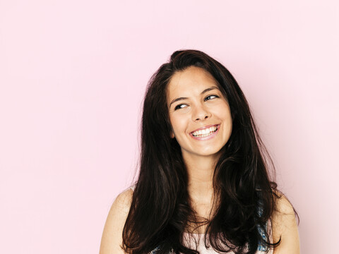 Porträt einer jungen lächelnden Frau mit schwarzen Haaren vor einem rosa Hintergrund, lizenzfreies Stockfoto