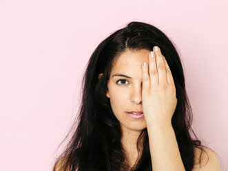 Portrait of young woman with black hair, eye covered in front of pink background - HMEF00357