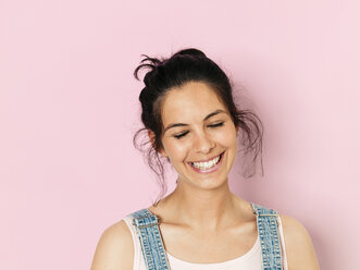 Porträt einer jungen lächelnden Frau mit schwarzen Haaren vor einem rosa Hintergrund - HMEF00365