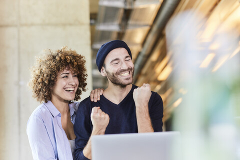 Aufgeregter Mann und Frau mit Laptop in einem modernen Büro, lizenzfreies Stockfoto