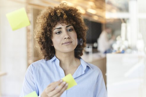 Businesswoman brainstorming with post-its on glass pane - FMKF05644