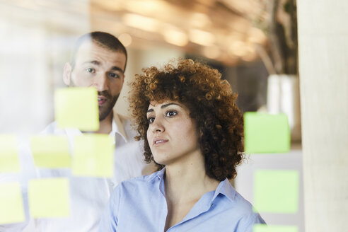 Zwei Kollegen beim Brainstorming mit Post-its auf einer Glasscheibe - FMKF05645