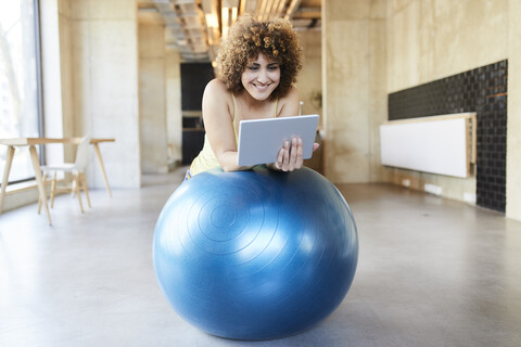 Lächelnde Frau, die ein Tablet auf einem Fitnessball in einem modernen Büro benutzt, lizenzfreies Stockfoto