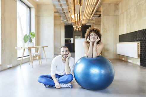 Porträt eines Mannes und einer Frau mit Fitnessball in einem modernen Büro - FMKF05653