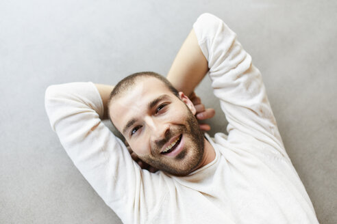 Porträt eines glücklichen jungen Mannes, der auf dem Boden liegt - FMKF05654