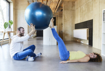 Glücklicher Mann und Frau üben mit Fitnessball in modernem Büro - FMKF05655