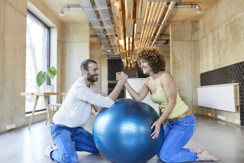 Glücklicher Mann und Frau Armdrücken auf Fitnessball in modernem Büro - FMKF05656