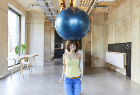 Porträt einer lächelnden Frau, die einen Fitnessball auf ihrem Kopf balanciert, lizenzfreies Stockfoto