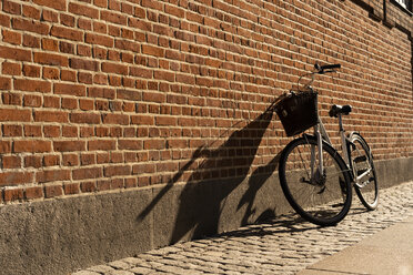 Dänemark, Kopenhagen, Fahrrad gegen Backsteinmauer gelehnt im Sonnenlicht - AFVF02730