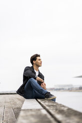 Denmark, Copenhagen, young man sitting at the waterfront - AFVF02740