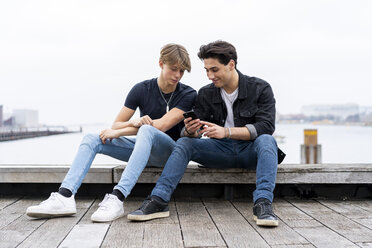 Dänemark, Kopenhagen, zwei junge Männer sitzen am Wasser und telefonieren - AFVF02750