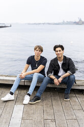 Dänemark, Kopenhagen, Porträt von zwei selbstbewussten jungen Männern, die am Wasser sitzen - AFVF02752