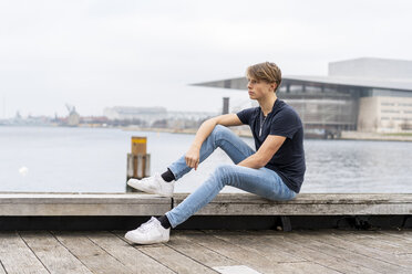 Dänemark, Kopenhagen, junger Mann sitzt am Wasser - AFVF02754