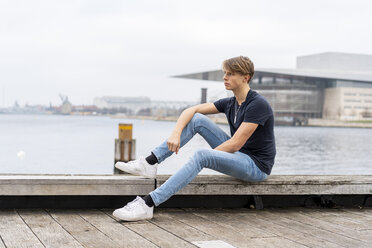 Denmark, Copenhagen, young man sitting at the waterfront - AFVF02754