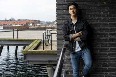 Denmark, Copenhagen, portrait of confident young man leaning against a wall at the waterfront - AFVF02760