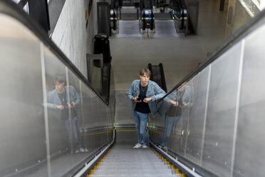 Junger Mann mit Mobiltelefon auf Rolltreppe - AFVF02766