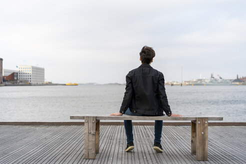 Dänemark, Kopenhagen, Rückansicht eines jungen Mannes, der auf einer Bank am Wasser sitzt - AFVF02776
