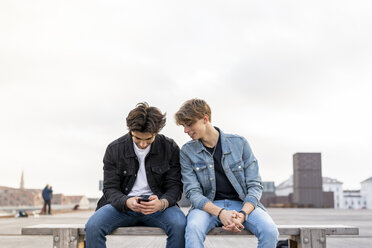 Dänemark, Kopenhagen, zwei junge Männer sitzen auf einer Bank und telefonieren - AFVF02782