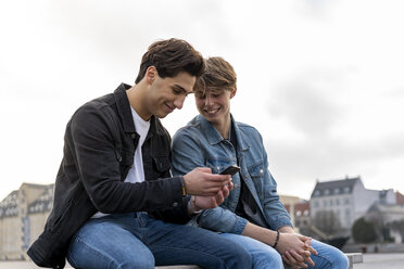 Dänemark, Kopenhagen, zwei junge Männer sitzen auf einer Bank und telefonieren - AFVF02784