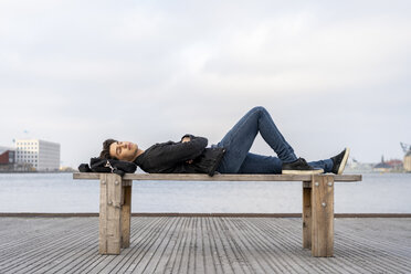 Denmark, Copenhagen, young man lying on a bench at the waterfront - AFVF02788