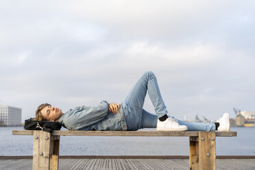 Denmark, Copenhagen, young man lying on a bench at the waterfront - AFVF02794