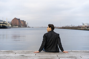 Dänemark, Kopenhagen, Rückansicht eines jungen Mannes, der am Wasser sitzt - AFVF02795