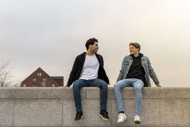 Denmark, Copenhagen, two young men sitting on a wall talking - AFVF02800