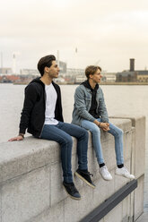 Dänemark, Kopenhagen, zwei junge Männer sitzen auf einer Mauer am Wasser - AFVF02802