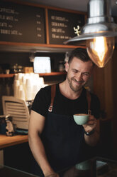 Smiling barista holding a coffee cup in coffee shop - OCMF00423