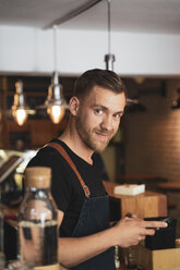 Portrait of smiling barista using mobile phone in coffee shop - OCMF00425