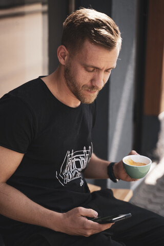 Junger Mann trinkt Kaffee und benutzt ein Mobiltelefon in einem Café, lizenzfreies Stockfoto