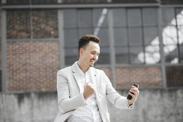 Porträt eines lächelnden Geschäftsmannes mit Smartphone - KMKF00865
