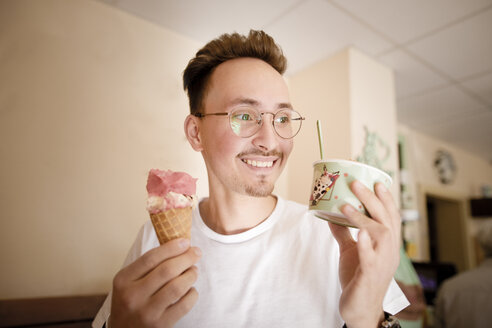 Porträt eines jungen Mannes mit Eiscreme in einer Eisdiele - KMKF00870