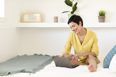 Smiling young woman using laptop in bed - JSMF01019