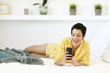 Smiling young woman using cell phone in bed - JSMF01025