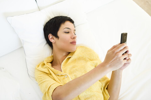 Junge Frau benutzt Mobiltelefon im Bett, lizenzfreies Stockfoto