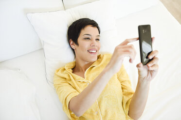 Lächelnde junge Frau mit Handy im Bett - JSMF01033