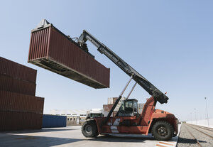 Kran hebt Frachtcontainer in der Nähe von Eisenbahnschienen auf einem Industriegelände - AHSF00166