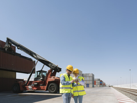 Arbeiter mit Tablet vor einem Kran mit Frachtcontainer auf einem Industriegelände, lizenzfreies Stockfoto