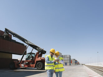 Arbeiter mit Tablet vor einem Kran mit Frachtcontainer auf einem Industriegelände - AHSF00173