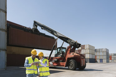 Arbeiter mit Tablet vor einem Kran mit Frachtcontainer auf einem Industriegelände - AHSF00174