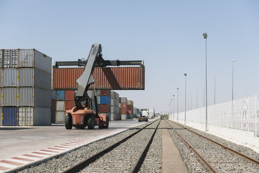 Kran hebt Frachtcontainer in der Nähe von Eisenbahnschienen auf einem Industriegelände - AHSF00176