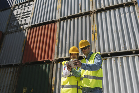 Arbeiter mit Tablet vor Frachtcontainern auf einem Industriegelände, lizenzfreies Stockfoto