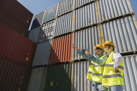 Arbeiter mit Tablet vor Frachtcontainern auf einem Industriegelände, lizenzfreies Stockfoto