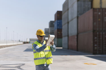 Arbeiter mit einem Notizblock in der Nähe von Frachtcontainern auf einem Industriegelände - AHSF00184