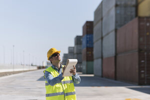 Arbeiter mit einem Notizblock in der Nähe von Frachtcontainern auf einem Industriegelände - AHSF00185