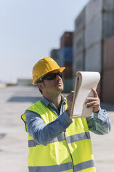 Arbeiter mit einem Notizblock in der Nähe von Frachtcontainern auf einem Industriegelände - AHSF00186