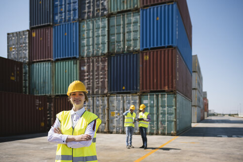 Portrait of confident female worker in front of colleagues and cargo containers on industrial site - AHSF00189