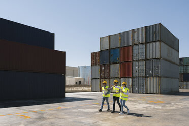 Arbeiter gehen zusammen in der Nähe eines Stapels von Frachtcontainern auf einem Industriegelände - AHSF00192