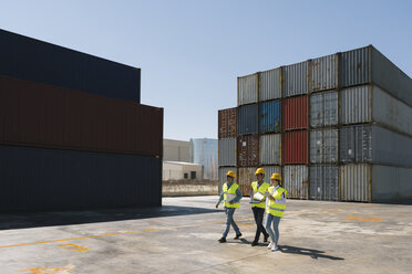Arbeiter gehen zusammen in der Nähe eines Stapels von Frachtcontainern auf einem Industriegelände - AHSF00193